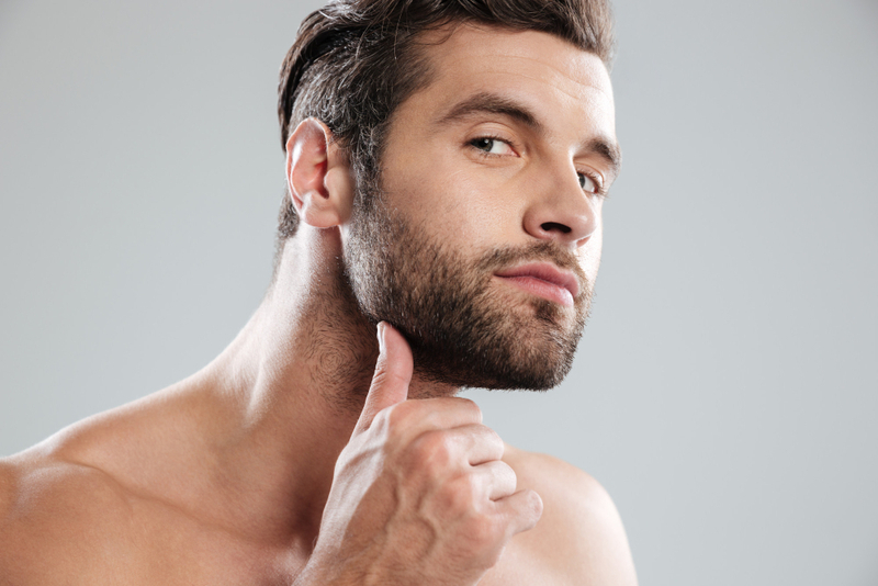 Portrait handsome naked bearded man examining his face